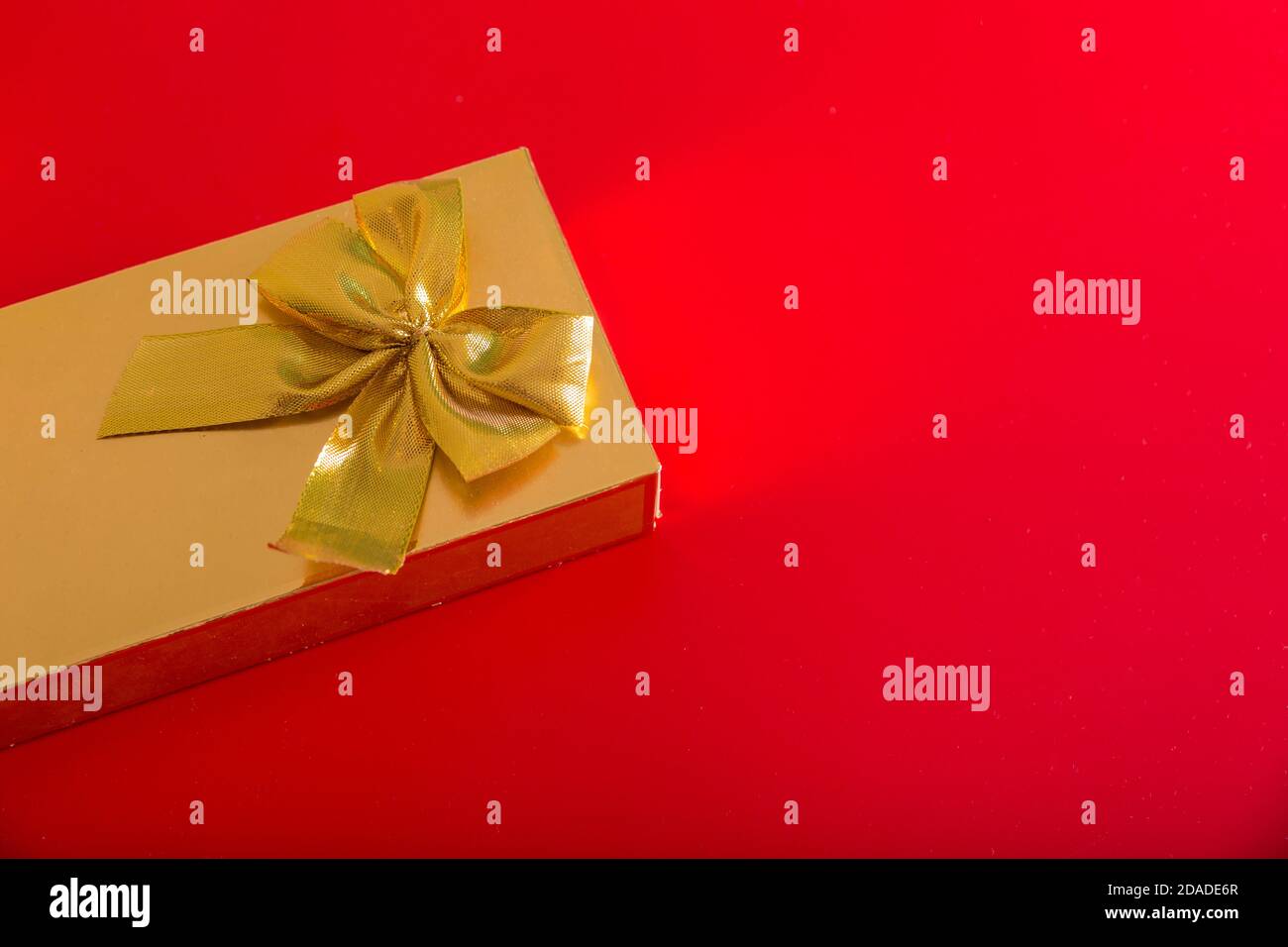 Geschenk in goldener Verpackung mit Schleife auf rotem Hintergrund Stockfoto