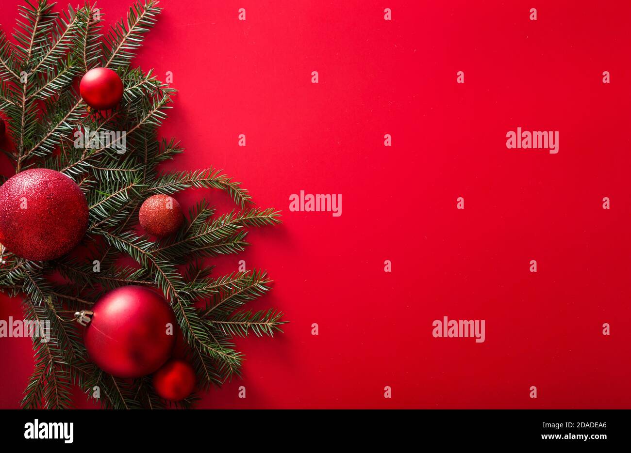 Christbaumzweige und rote Neujahrskugeln auf rotem Hintergrund. Stockfoto