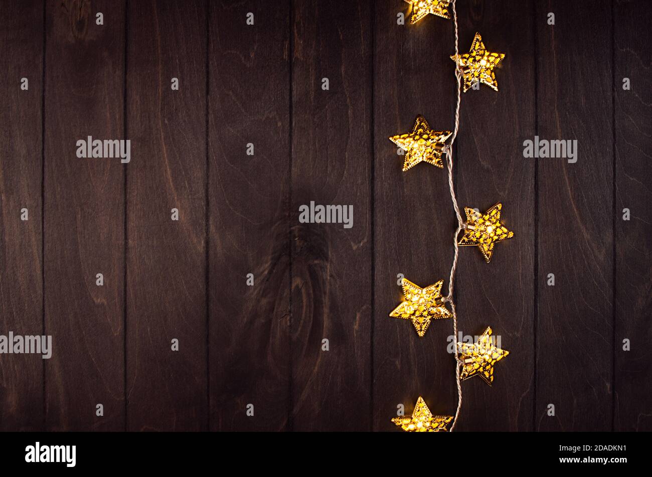 Weihnachtsdekoration - goldene Sterne auf Lichtern Girlande glühen auf dunkelbrauner Planke, Bordüre, Draufsicht, Kopierraum, vertikal. Stockfoto