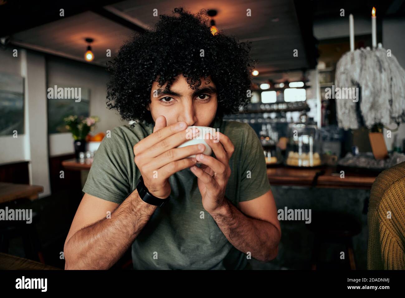 Schöner junger Mann mit lockigen Haaren nippen heißen Kaffee entspannend Im Café Stockfoto