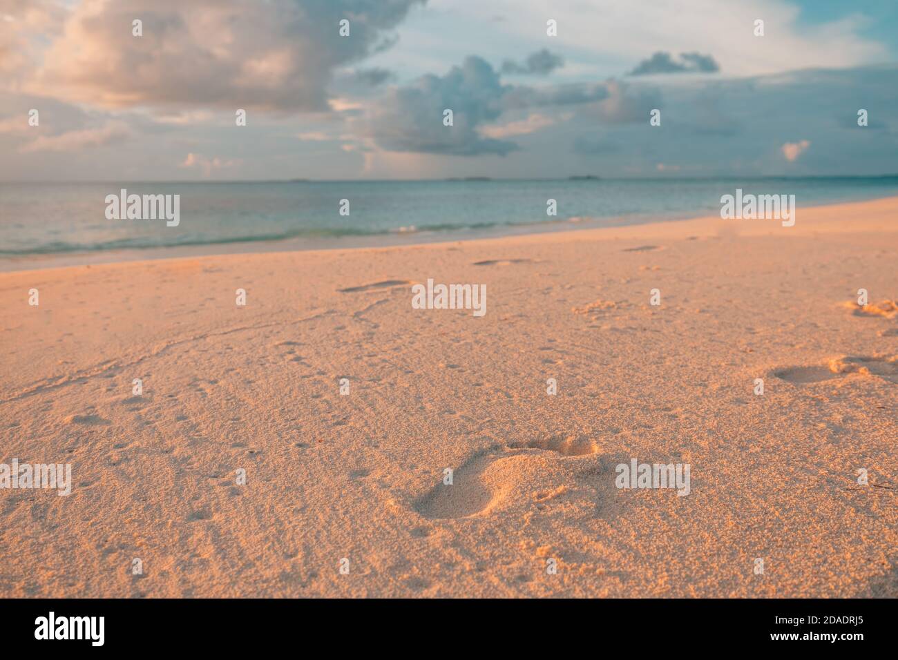 Friedlicher Strand, Wellen und Fußstapfen bei Sonnenuntergang. Fußabdrücke bei Sonnenuntergang mit goldenem Sand. Strand, Welle, Zukunftsziele Konzept. Idyllische Naturlandschaft Stockfoto