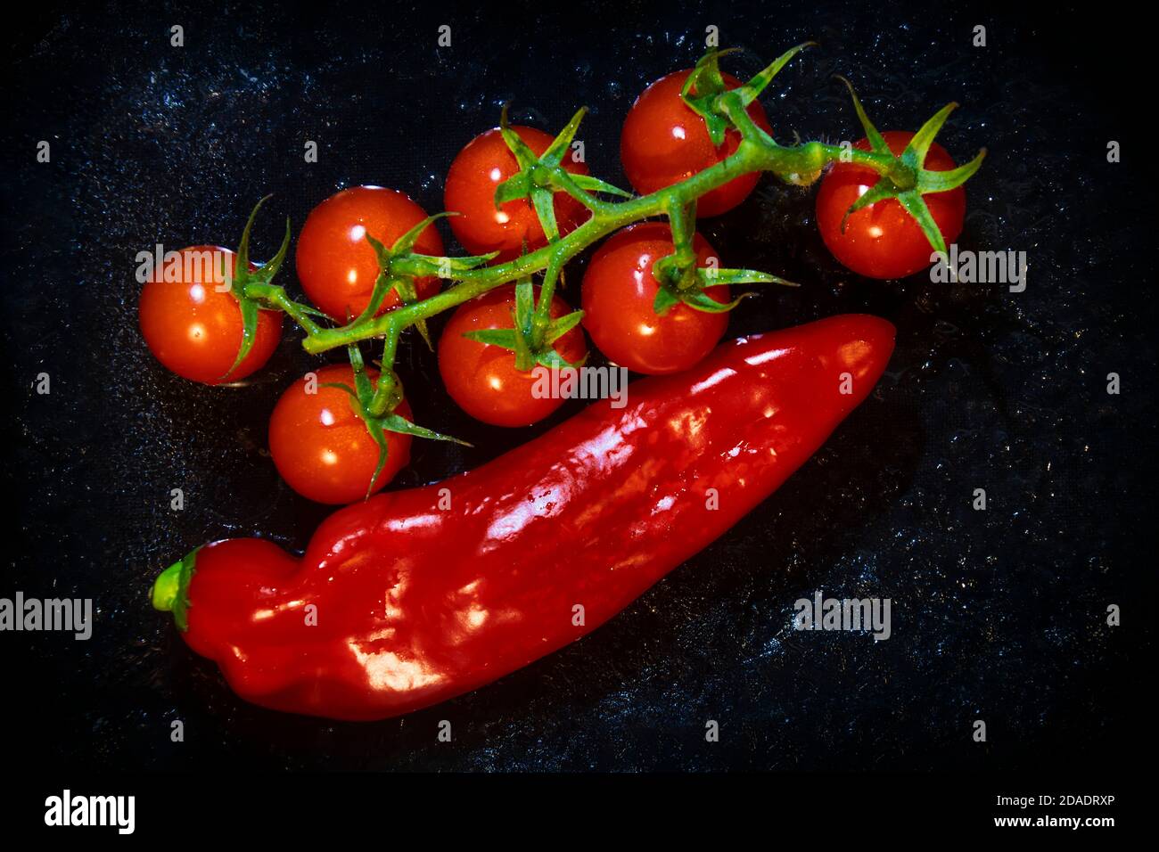 Rote Paprika und Rebe von Tomaten auf dem schwarzen Eis. Stockfoto