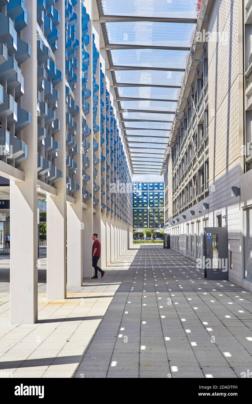 Licht und Schatten in architektonischer Perspektive auf dem Parkplatz in Milton Keynes mit einem jüngeren Mann, der eine Gesichtsbedeckung trägt Stockfoto