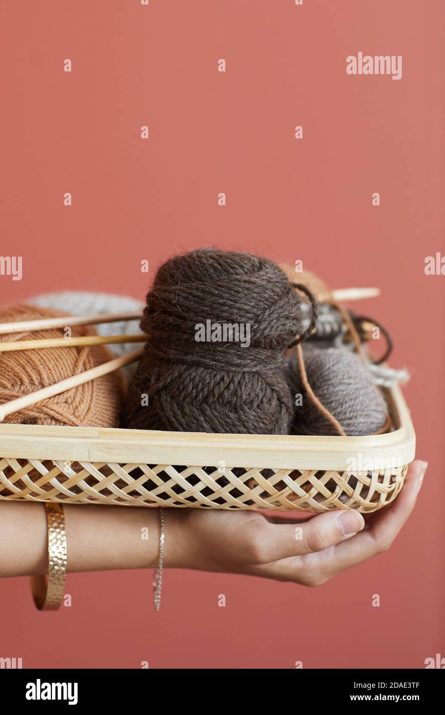 Nahaufnahme einer Frau, die den Korb mit Wolle und Stricknadeln hält Zum Stricken isoliert auf rosa Hintergrund arbeiten Stockfoto