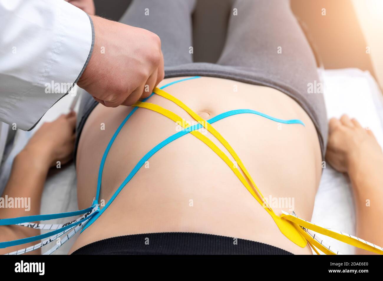 Männlicher Physiotherapeut, der gelbes klebendes elastisches therapeutisches Band auf das Weibchen auflegt Bauchmuskel von jungen Erwachsenen schlank sportliche Frau liegend auf Tisch Stockfoto