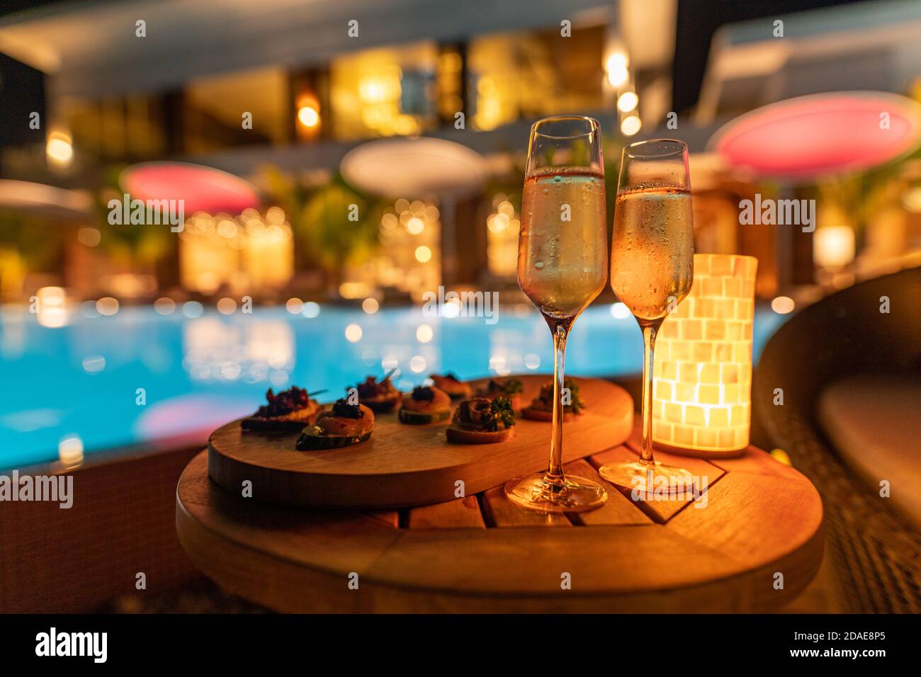 Romantische Gläser Champagner auf verschwommenem Luxus Resort Pool Hintergrund des Sonnenuntergangs. LED-Leuchten, romantisches Paar Vorspeise, Ruhe, Nachtstimmung Stockfoto