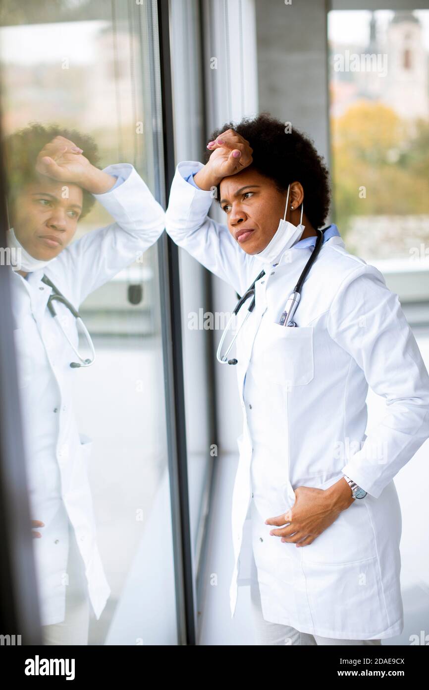 Schwarze Ärztin steht neben dem Arztpraxis Fenster mit Negativer Ausdruck Stockfoto
