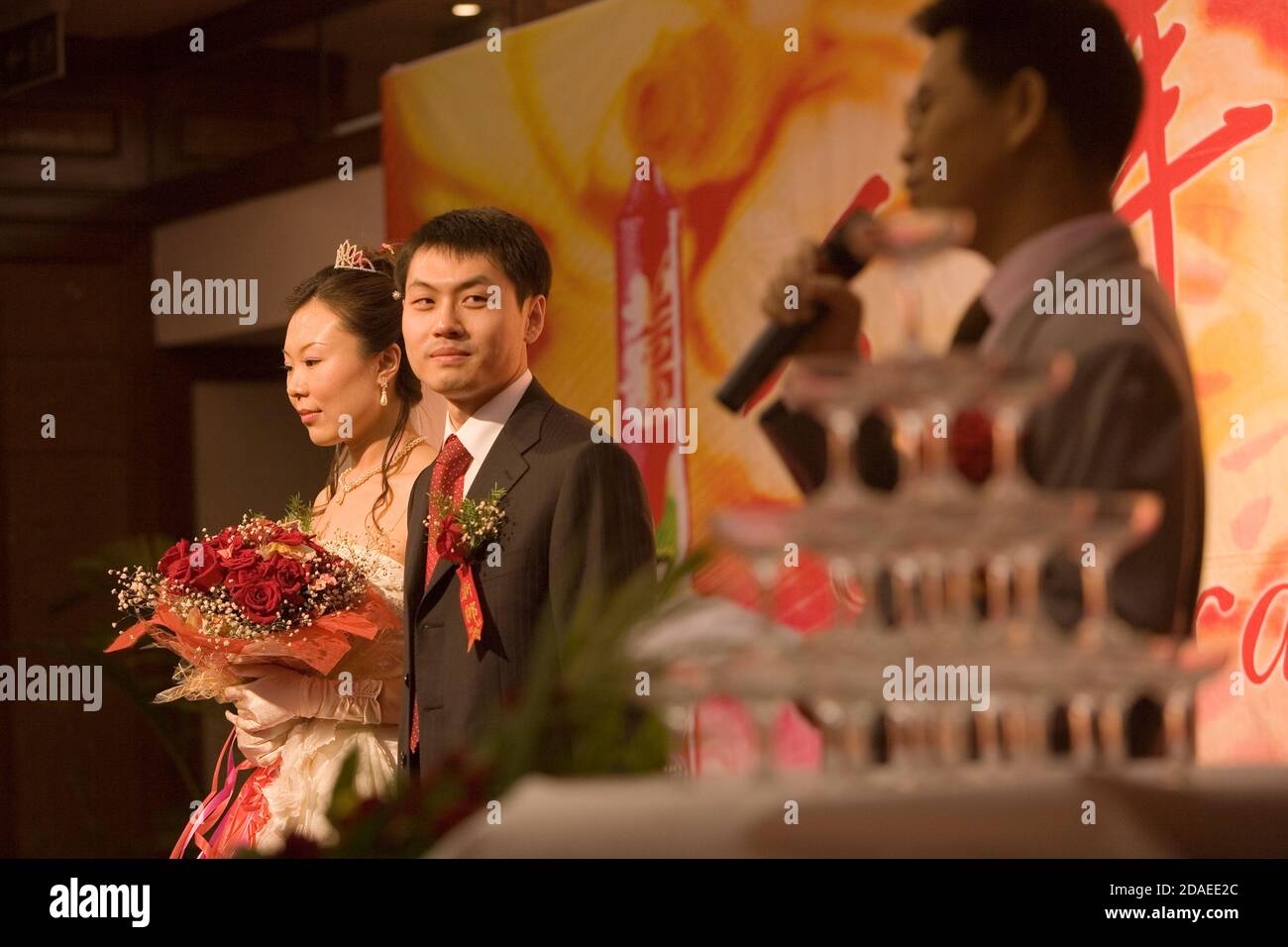 PEKING, CHINA - 2006. JUNI: Braut Cheng Hui und Bräutigam Zhao Jun, beide 28, stehen auf der Bühne, während der beste Mann seine Rede hält. Sie trafen sich während ihrer Arbeit bei KPMG, wo Zhao Jun Manager ist. Stockfoto