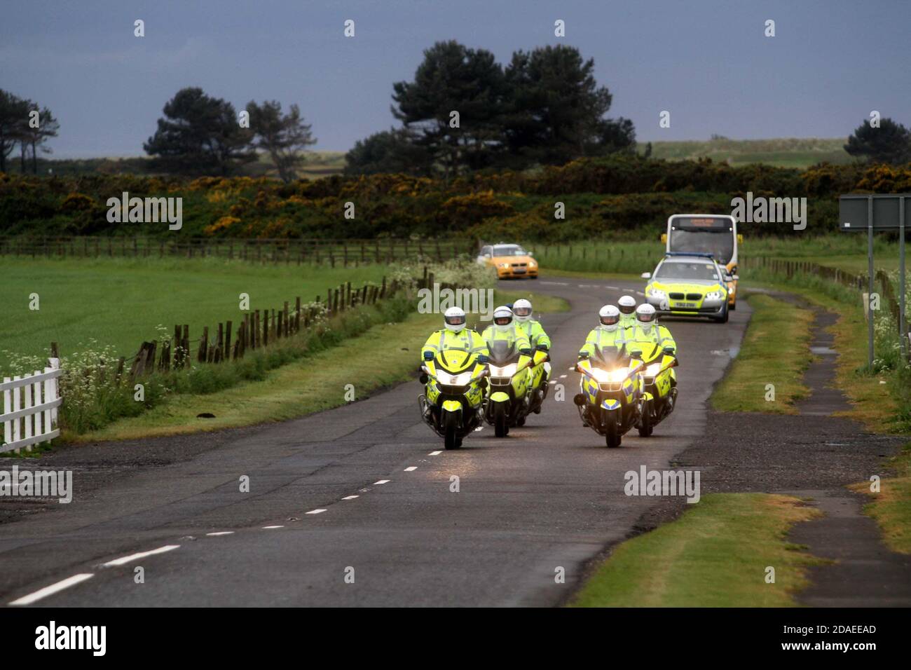 Ayrshire, Schottland, Großbritannien. Die London 2012 Olympic Fackel reist durch South Ayrshire, angefeuert von lokalen Gemeinden und Schulkindern. Die Autokolonne mit der Fackel und der Begleitmannschaft kommt mit Polizeieskorte in Maidens, Ayrshire an Stockfoto