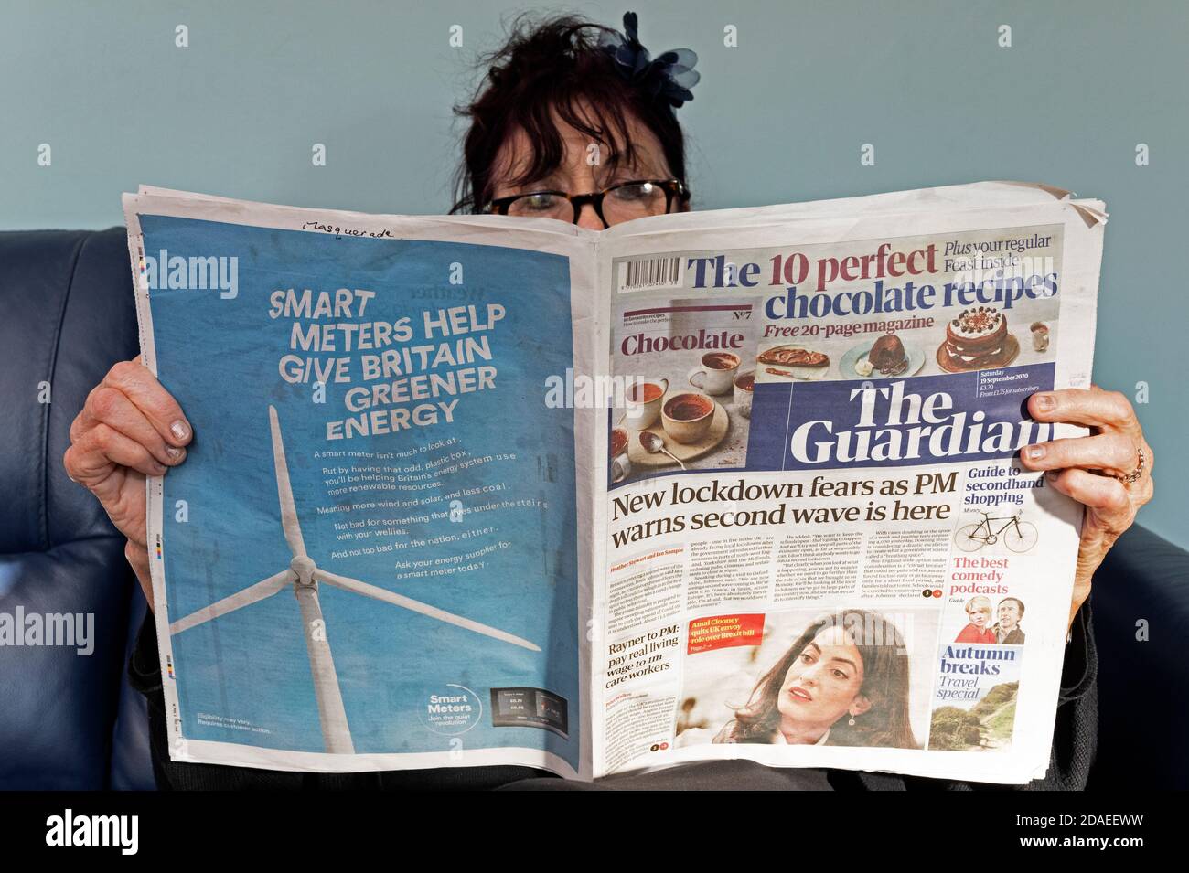Frau beim Lesen der Guardian Zeitung mit Schlagzeilen über Coronavirus an zweiter Stelle Winken Stockfoto