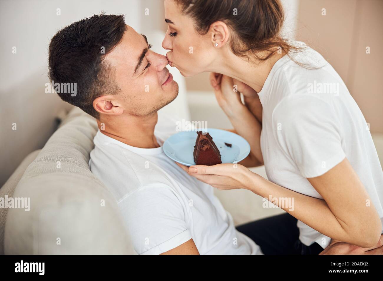 Liebevolle Frau hält Teller mit Kuchen und küsst ihren Mann Stockfoto