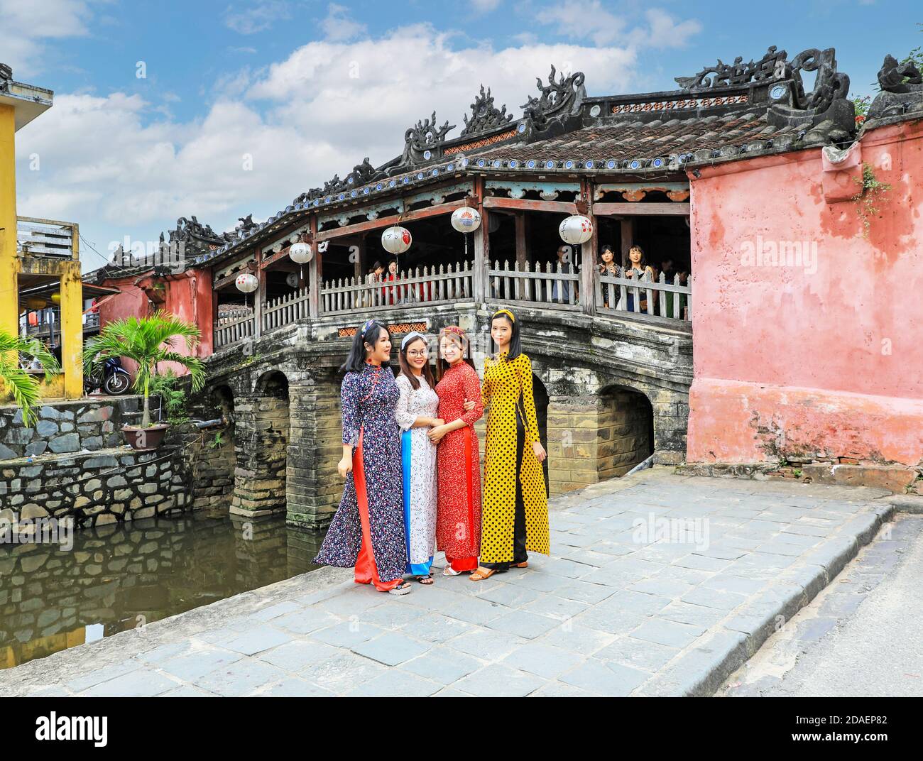 Vier vietnamesische junge Damen in traditioneller Kleidung, die Ao dai, posieren für ein Foto an der japanischen überdachten Brücke, Hoi an, Vietnam, Asien Stockfoto