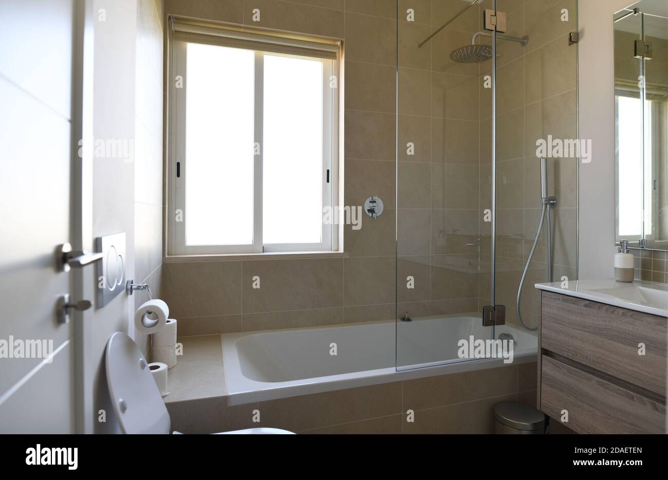 Neues Badezimmer mit Badewanne, Waschbecken und Duschabtrennwand mit beigefliesten Wänden Stockfoto