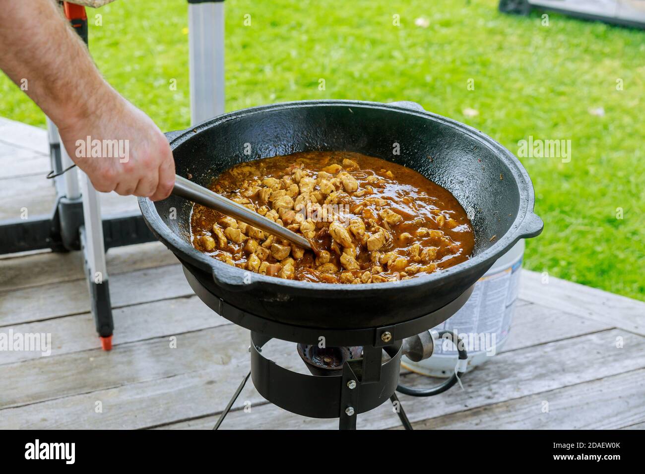 Mann Rühren Hühnerfleisch in Gusseisen Kessel im Freien. Stockfoto