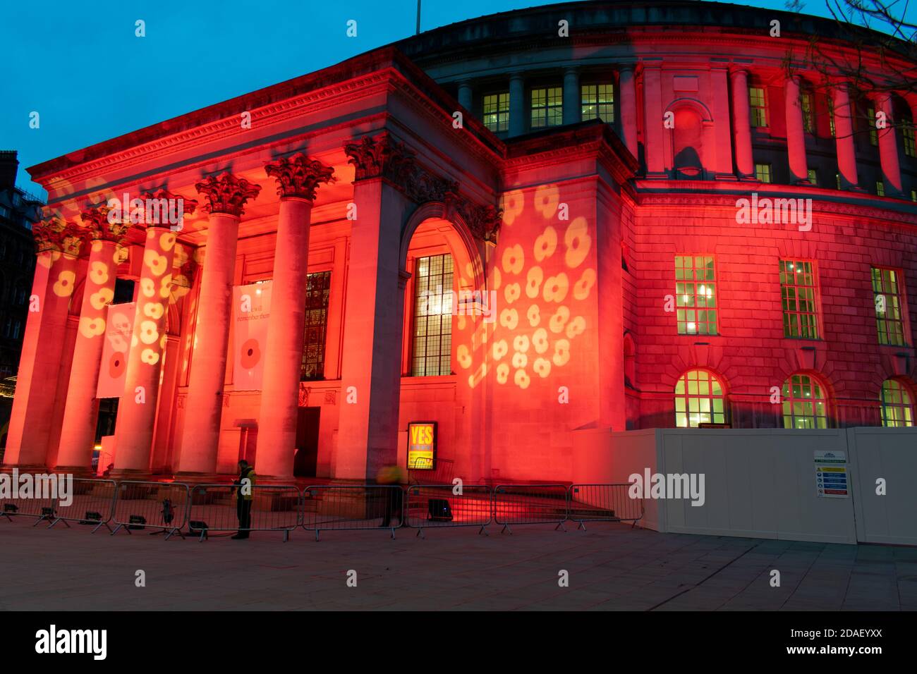 Waffenstillstandstag Gedenkfeier während der Aussperrung. Manchester Central Library, UK beleuchtet mit rotem Licht und Mohn-Design. Verschwommene Menschen. Öffentliches Gebäude Stockfoto