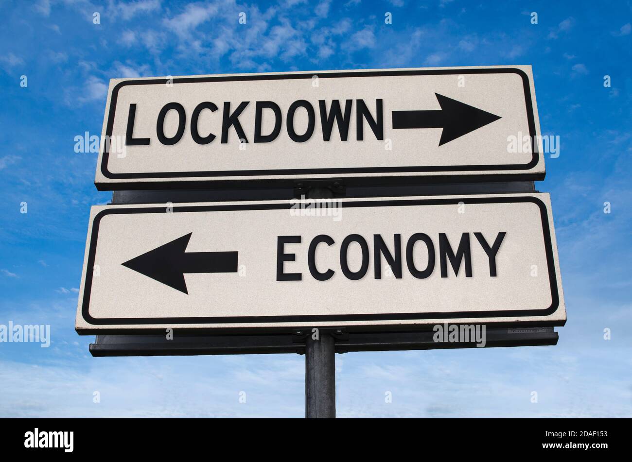 Lockdown und Wirtschaft weiß zwei Pfeile Zeichen auf Metallstange. Richtungsstraße. Kreuzung Straßenschild, zwei Pfeile vor blauem Himmel Hintergrund. Zwei-Wege-Roa Stockfoto
