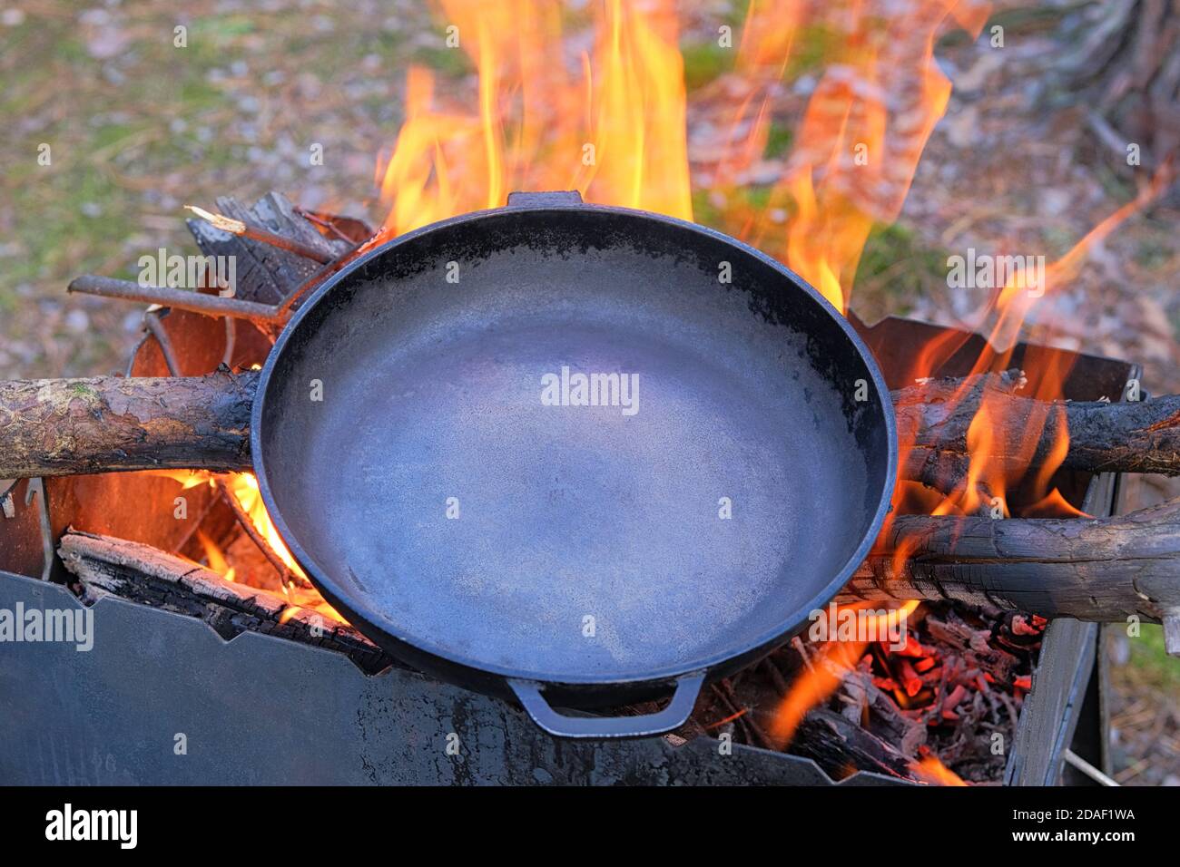 Gusseisen Pfanne über einem roten Feuer erhitzt sich für weitere Kochen.  Feuern einer gusseisernen Pfanne über einem offenen Feuer Stockfotografie -  Alamy