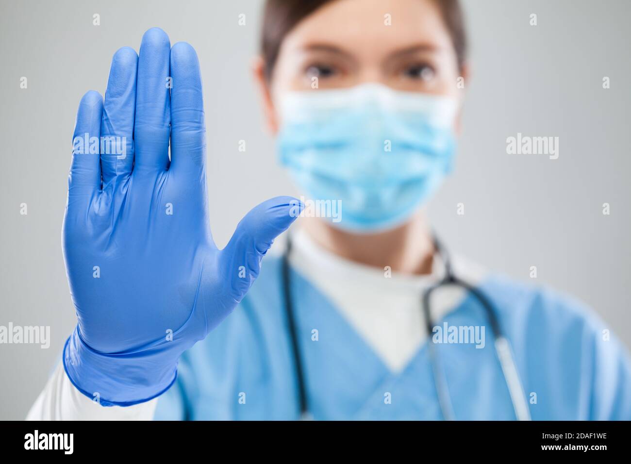 Junge weibliche UK NHS Intensivmedizin Arzt Hand gestikulieren STOPPEN Coronavirus COVID-19 Krankheit globaler Pandemieausbruch, bitte helfen Sie nicht Virus weltweit zu verbreiten Stockfoto