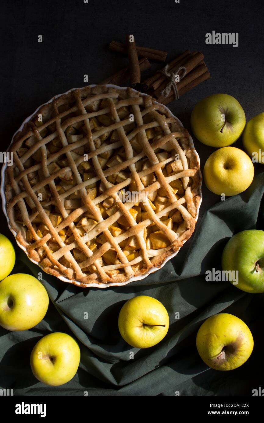 Apfelkuchen auf grünem Stoff Hintergrund. Frische gelbe Äpfel, Zimtstangen auf einem Tisch. Dessertideen für den Herbst. Stockfoto