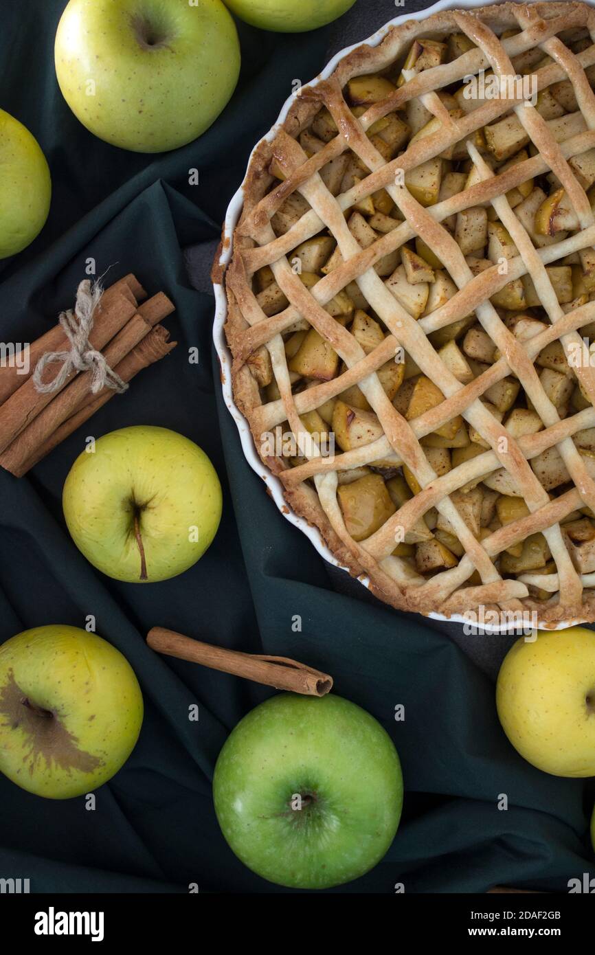 Apfelkuchen auf grünem Stoff Hintergrund. Frische gelbe Äpfel, Zimtstangen auf einem Tisch. Dessertideen für den Herbst. Stockfoto