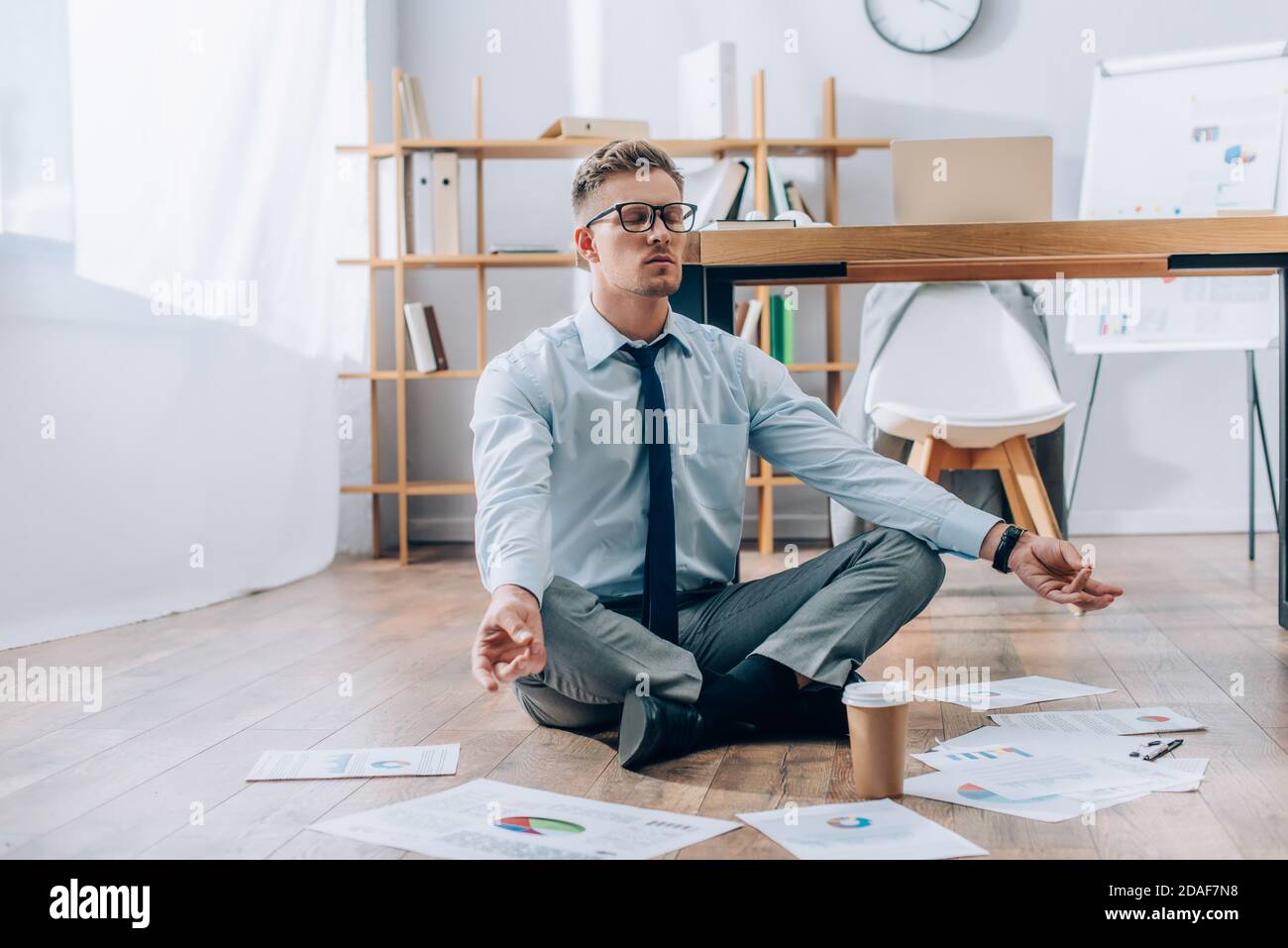 Junger Geschäftsmann meditiert in der Nähe von Zeitungen und Kaffee, um weiter zu gehen Etage im Büro Stockfoto