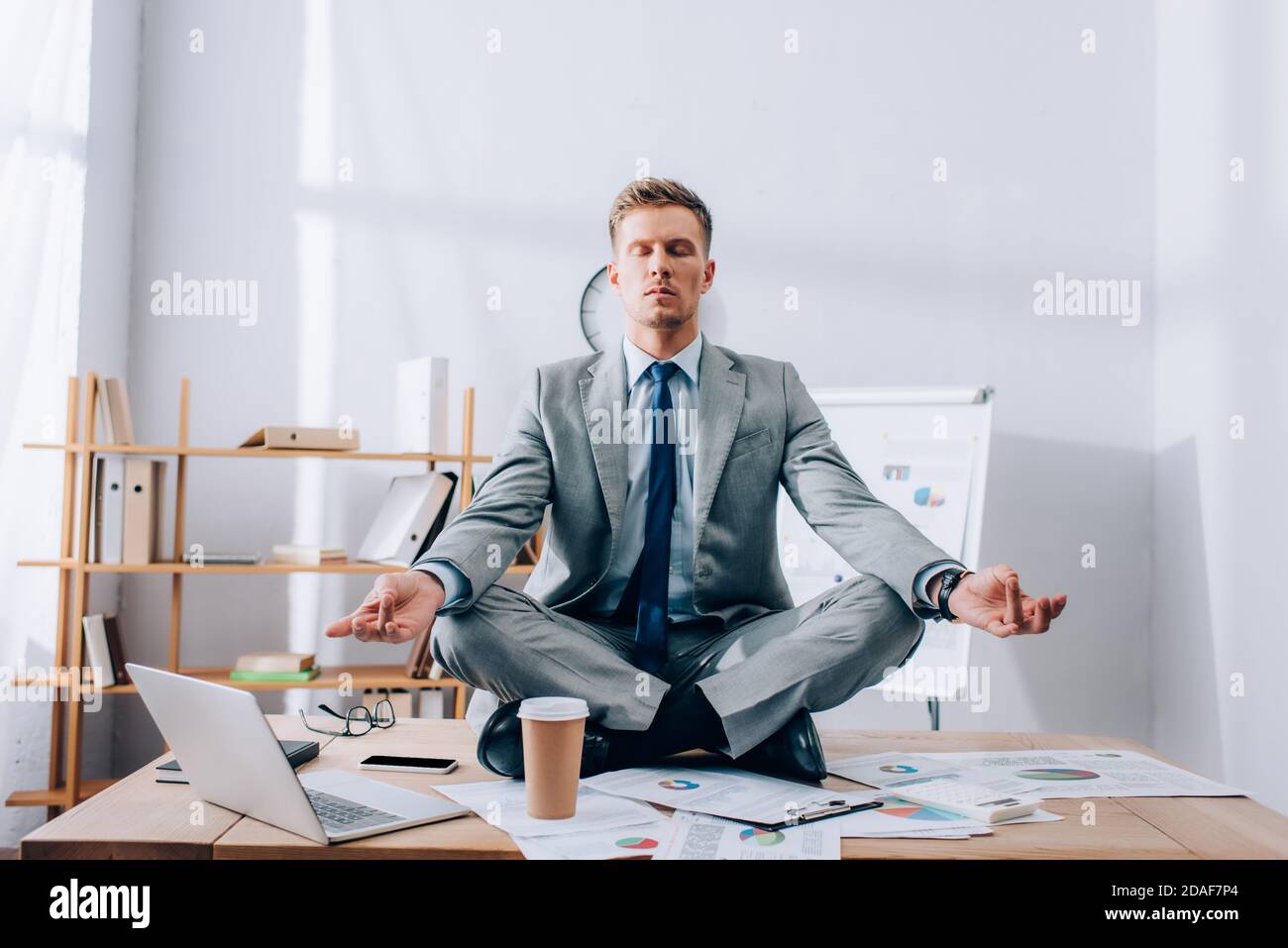Junger Geschäftsmann in Anzug meditiert in der Nähe von Zeitungen und Geräte auf Tabelle Stockfoto