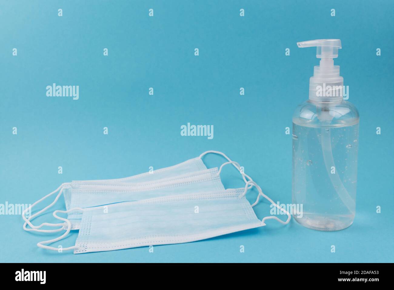 Einweg-Gesichtsmasken und Handdesinfektionsmittel in der Spenderflasche gegen Blauer Hintergrund Stockfoto