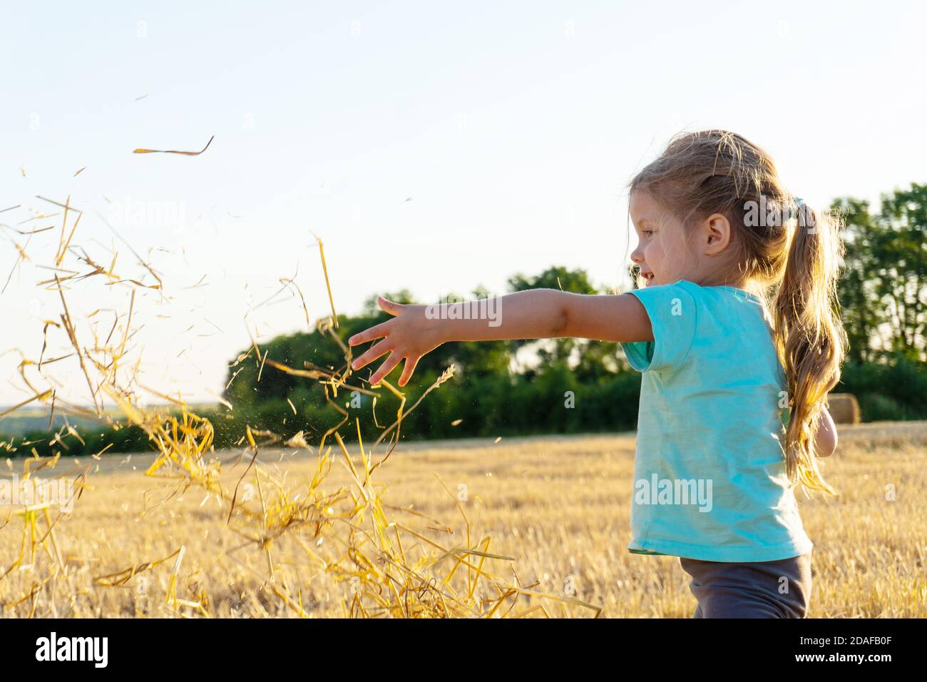 Kleines Mädchen spielt mit Weizengras auf dem Feld Stockfoto