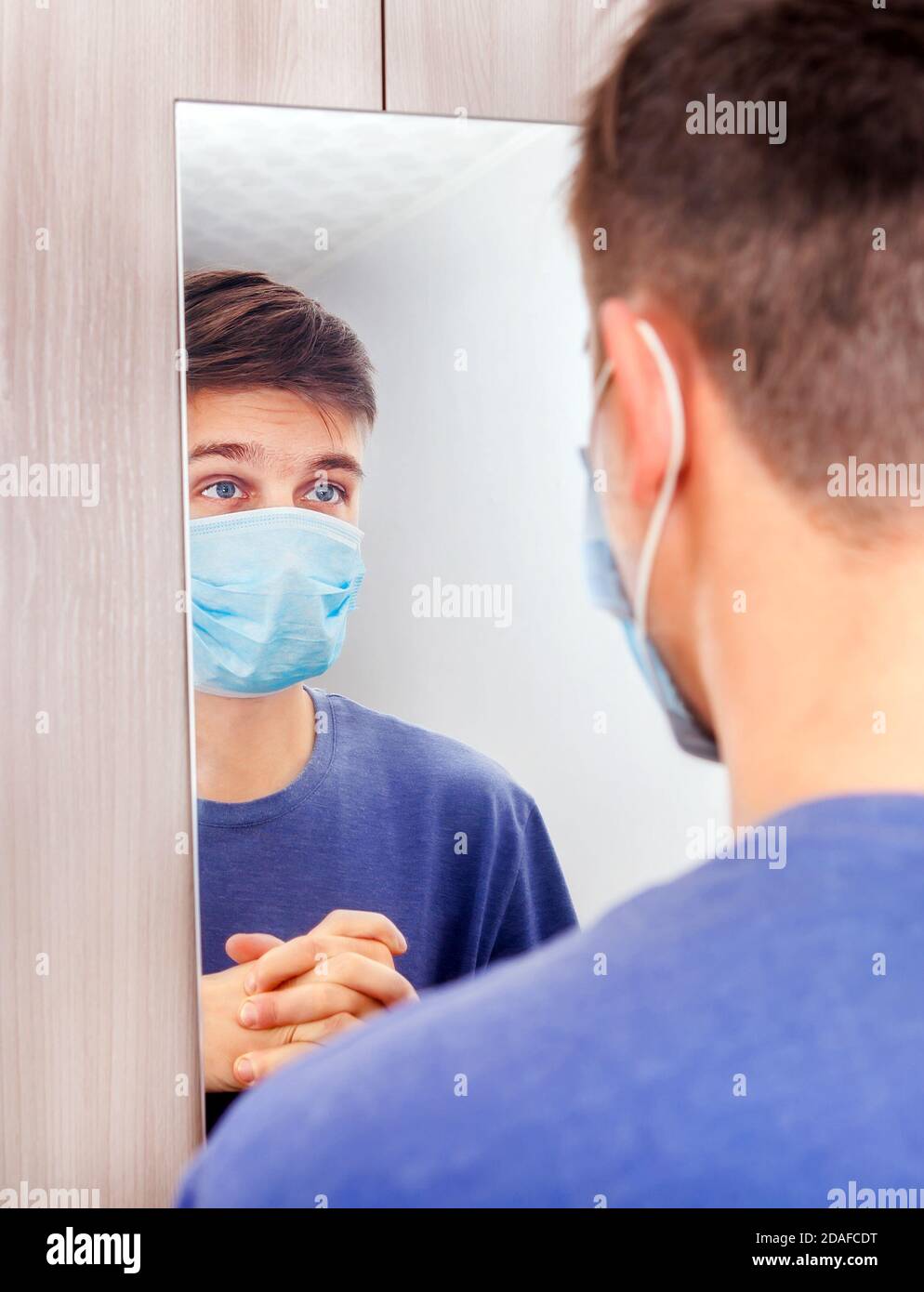 Junger Mann in Grippe-Maske Blick auf Reflexion in der Spiegel Stockfoto