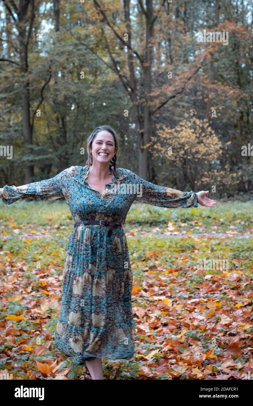 Glückliche Frau nass in einem Herbstwald mit langen Willam Morris Kleid, nur aus dem Wasser Stockfoto