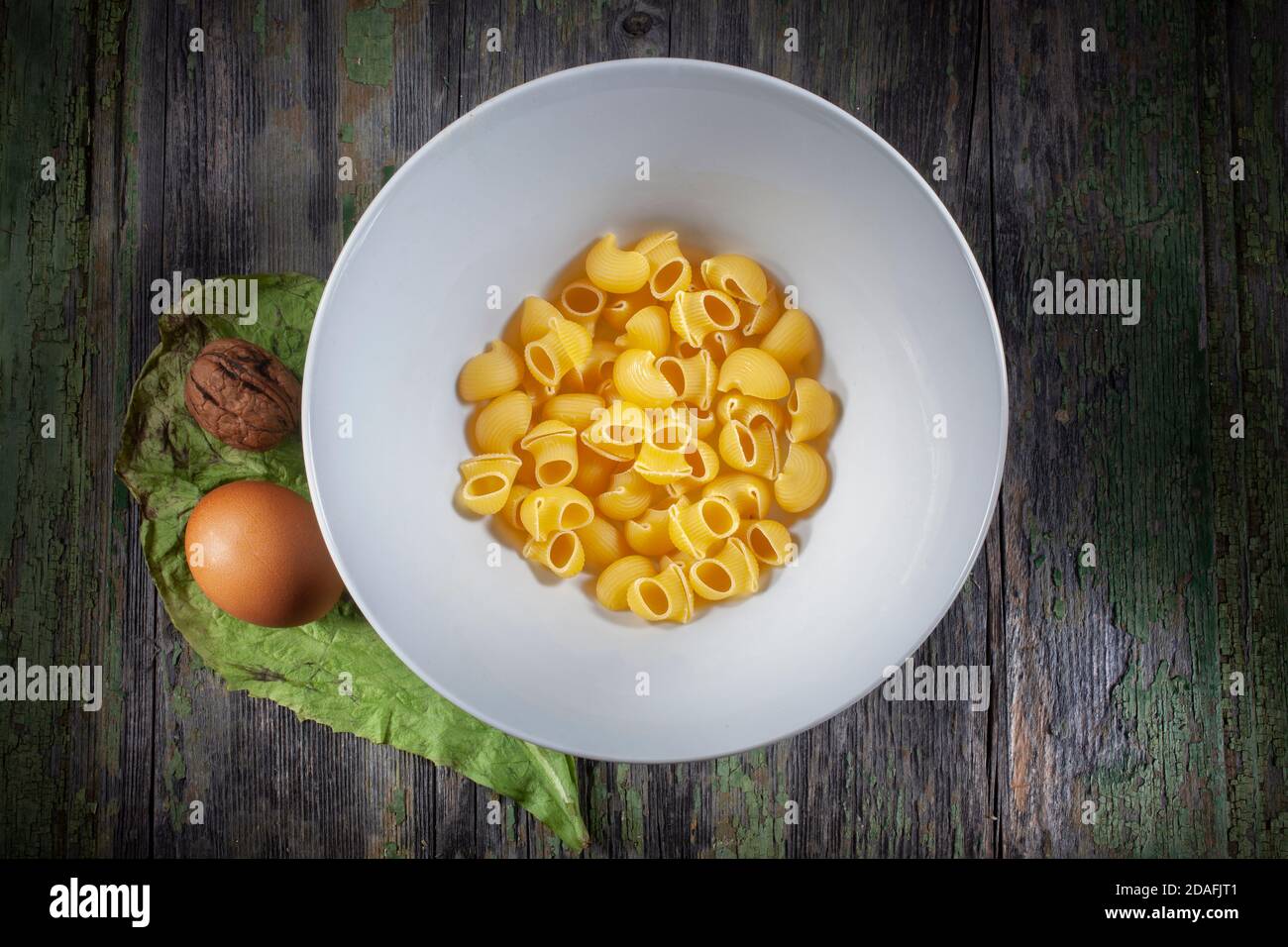 Makro-Foto von Vivid Raw Pasta in White Bowl auf Verfallener Holzhintergrund mit frischem Ei und Walnuss auf dekoriert Chicoriy Leaf Stockfoto