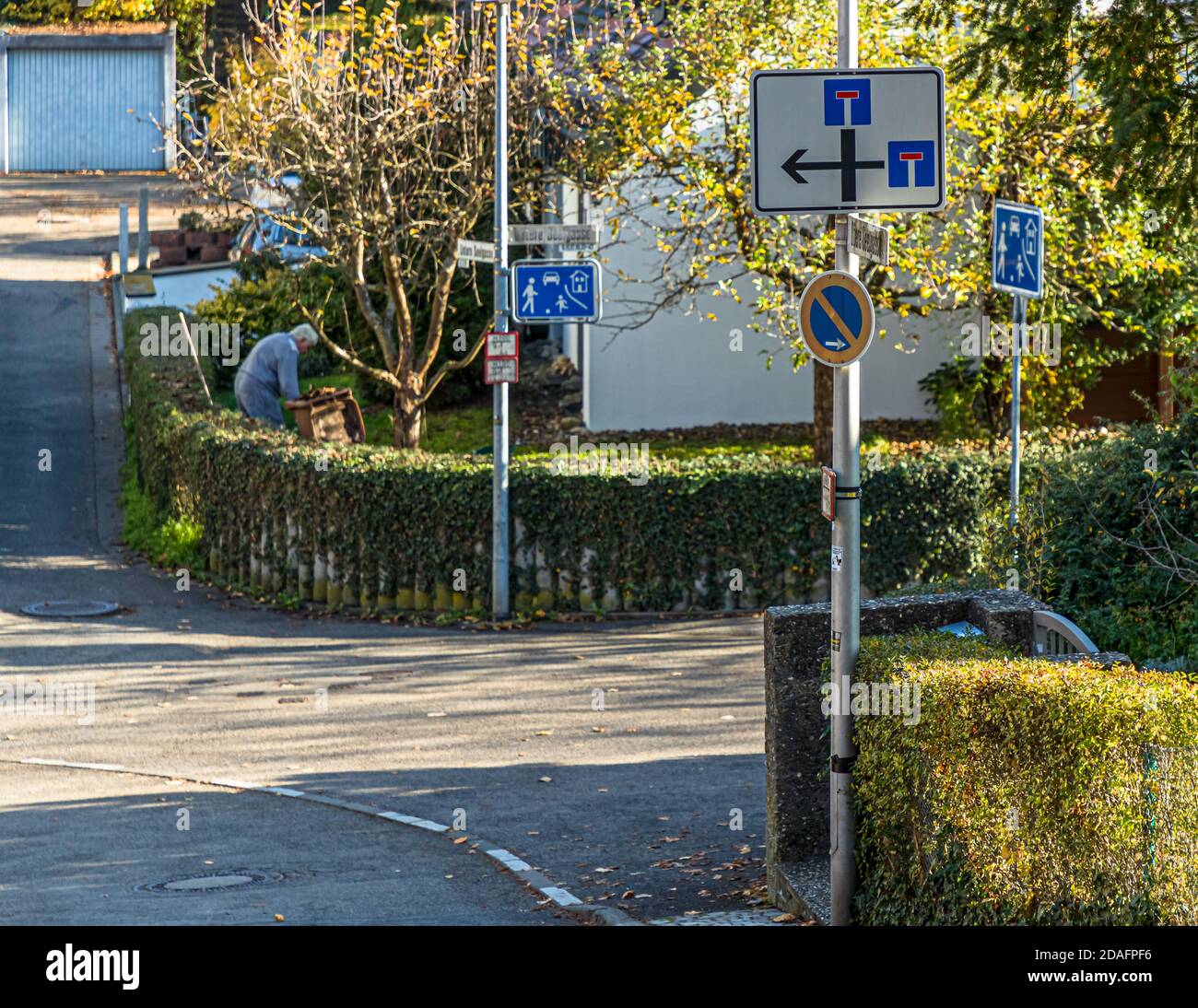 Sackgassen- und Spielstraßenschilder säumen eine ruhige Wohnstraße in einem Vorort von Bamberg, Bayern, Deutschland. Im Hintergrund arbeitet eine Person in Schutzkleidung in einem Vorgarten. Stockfoto