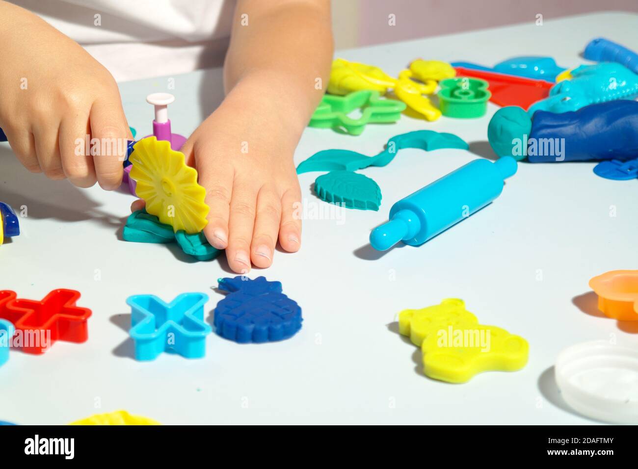 Kind spielt mit Spielteig auf dem blauen Tisch. Viele Spielzeuge auf dem Tisch Formen, Teigwalze und Schere. Glückliches Kind hat Spaß mit Spielzeug. Stockfoto