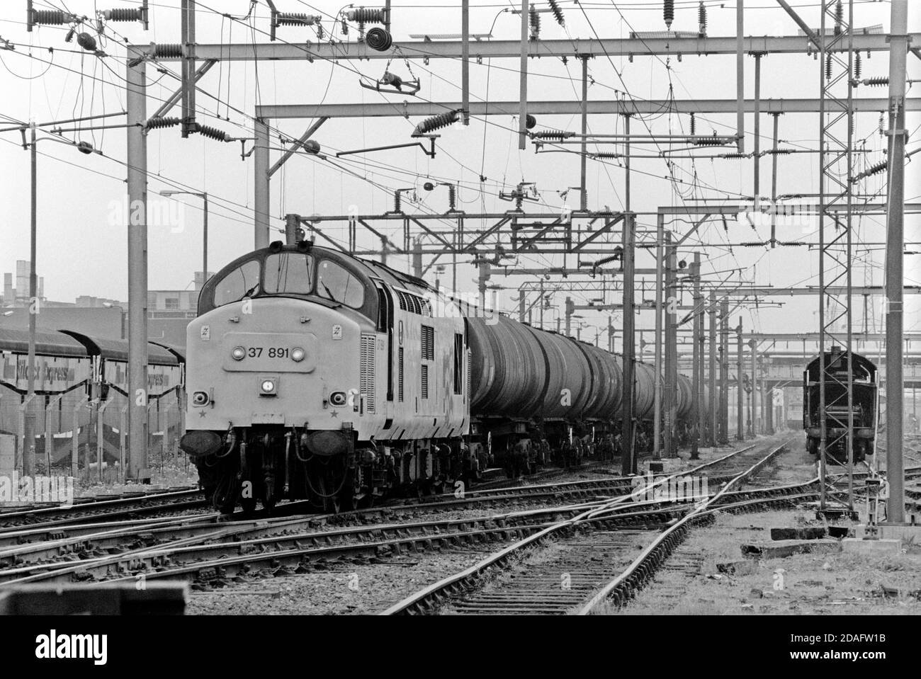 Am 25. Mai 1991 fährt eine Diesellokomotive der Baureihe 37 der Baureihe 37891 mit einem Zug aus Bogenöltanks an den Bahnhof Dagenham Dock. Stockfoto