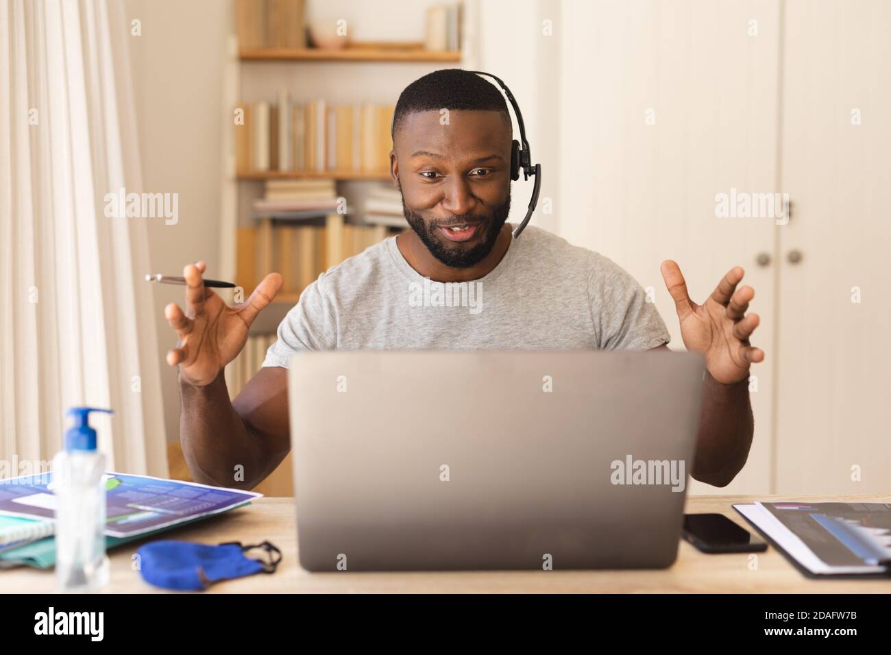 Afroamerikanischer Mann mit Telefon-Headset, während ein Video Chatten Sie auf dem Laptop, während Sie von zu Hause aus arbeiten Stockfoto