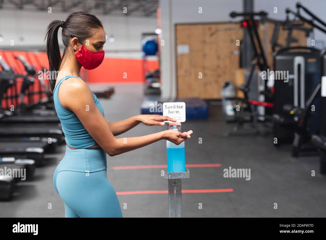 Passen kaukasische Frau trägt Gesichtsmaske desinfizieren ihre Hände in Der Fitnessraum Stockfoto