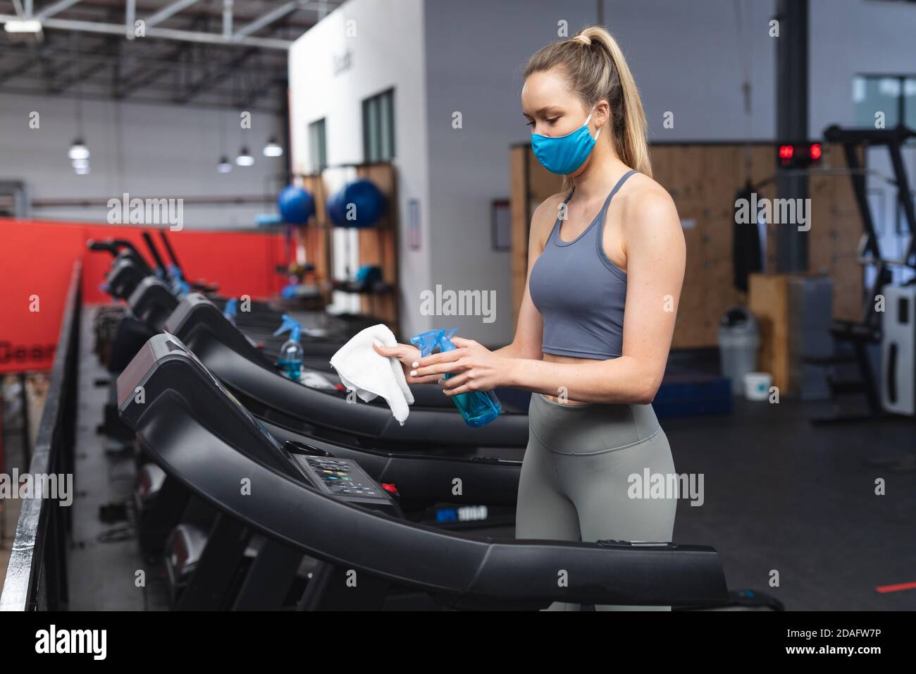 Fit kaukasische Frau trägt Gesichtsmaske desinfizieren Cardio-Maschine vor Trainieren im Fitnessraum Stockfoto