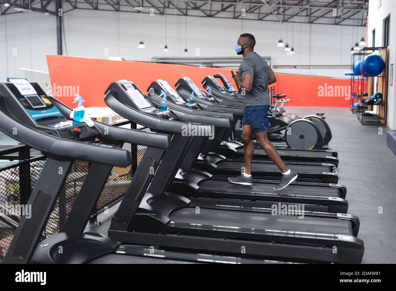 Fit afroamerikanischen Mann trägt Gesichtsmaske läuft auf Laufband Dabei Cardio-Training in der Turnhalle Stockfoto