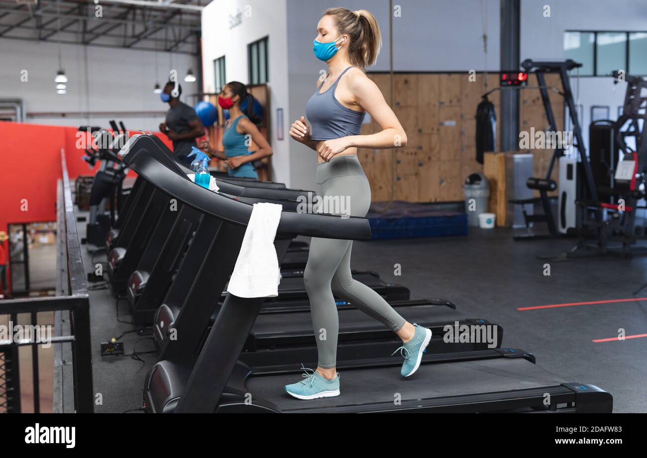 Fit kaukasische Frau trägt Gesichtsmaske läuft auf Laufband tun Cardio-Training im Fitnessstudio Stockfoto