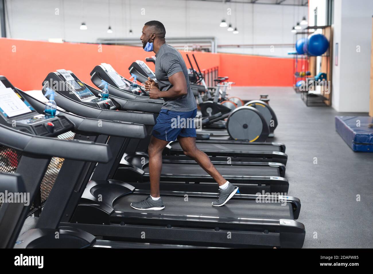 Fit afroamerikanischen Mann trägt Gesichtsmaske läuft auf Laufband Dabei Cardio-Training in der Turnhalle Stockfoto