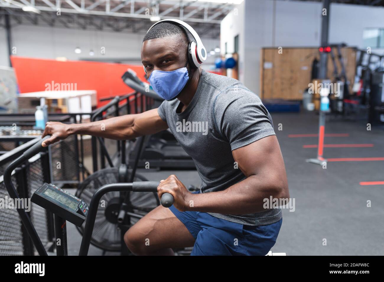 Portrait von fit afroamerikanischen Mann trägt Gesichtsmaske und Kopfhörer Training auf Heimtrainer Stockfoto