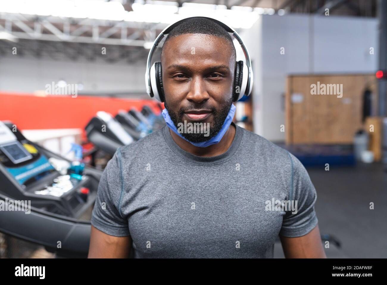 Portrait von fit afroamerikanischen Mann mit Gesichtsmaske herum Sein Hals trägt Kopfhörer in der Turnhalle Stockfoto