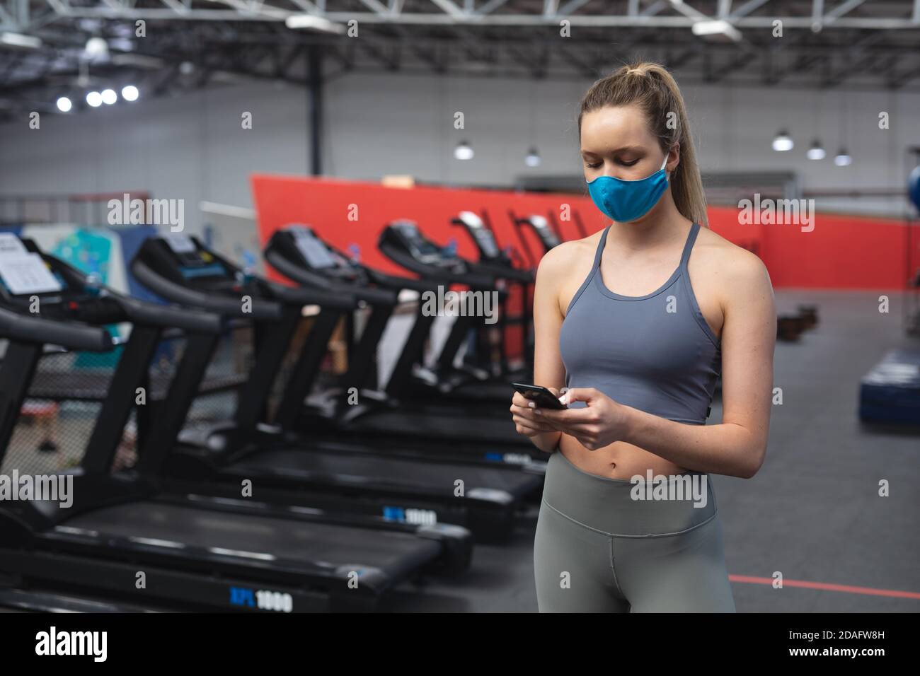 Passen kaukasische Frau trägt Gesichtsmaske mit Smartphone in der Fitnessraum Stockfoto