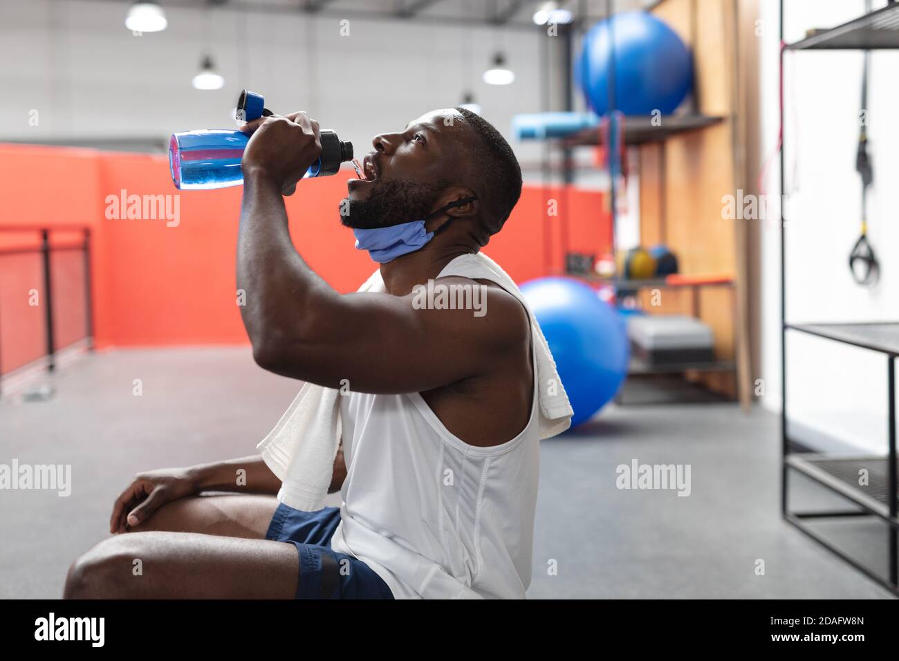 Fit afroamerikanischen Mann mit Gesichtsmaske um den Hals Trinkwasser im Fitnessraum Stockfoto
