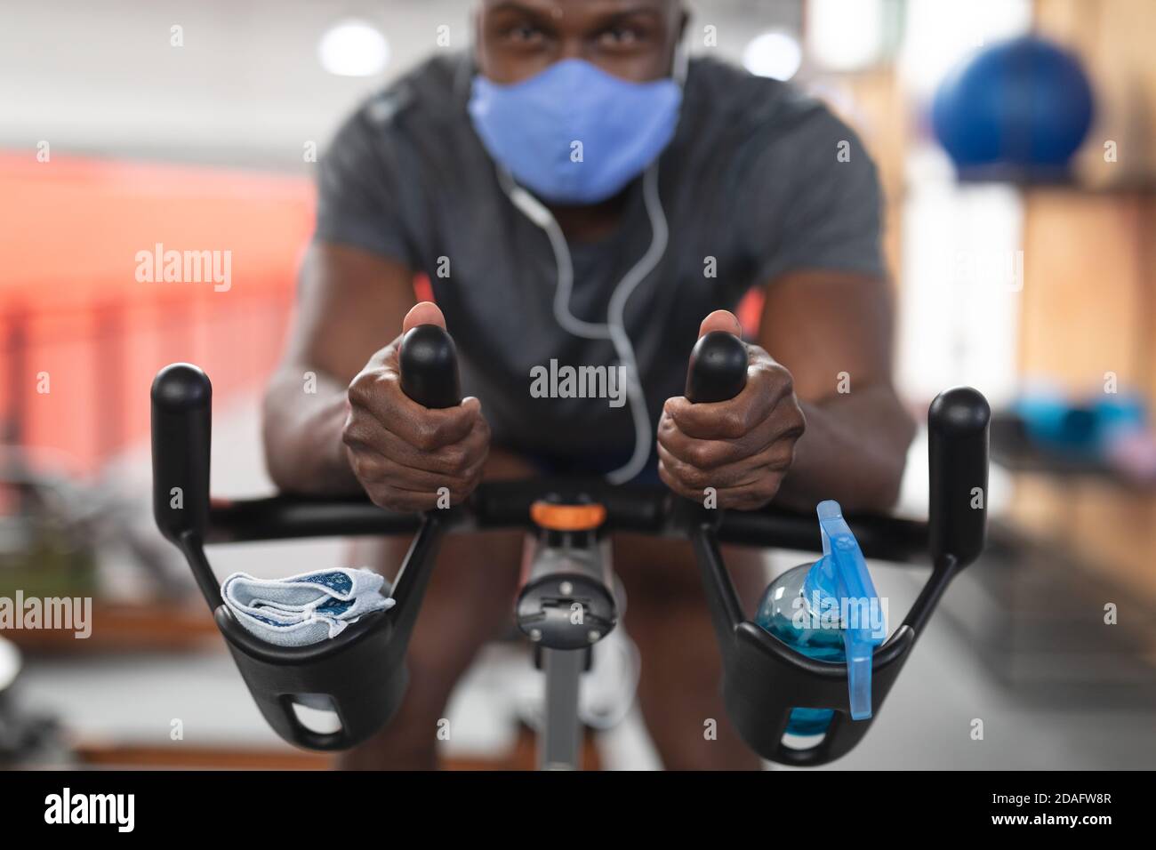 Portrait von fit afroamerikanischen Mann trägt Gesichtsmaske und Kopfhörer Training auf Heimtrainer i Stockfoto
