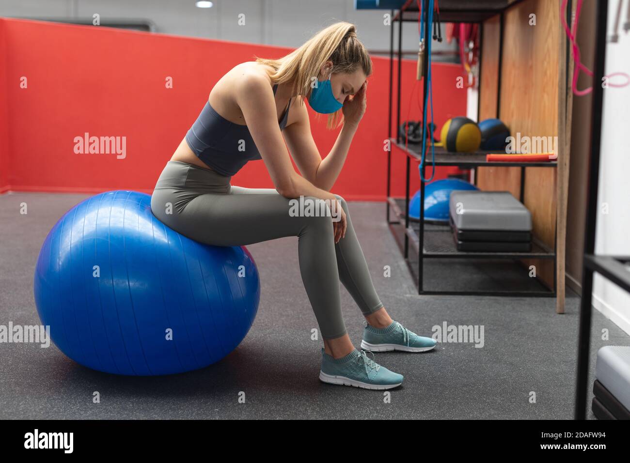 Gestresst fit kaukasische Frau trägt Gesichtsmaske sitzen bei der Übung Ball im Fitnessstudio Stockfoto