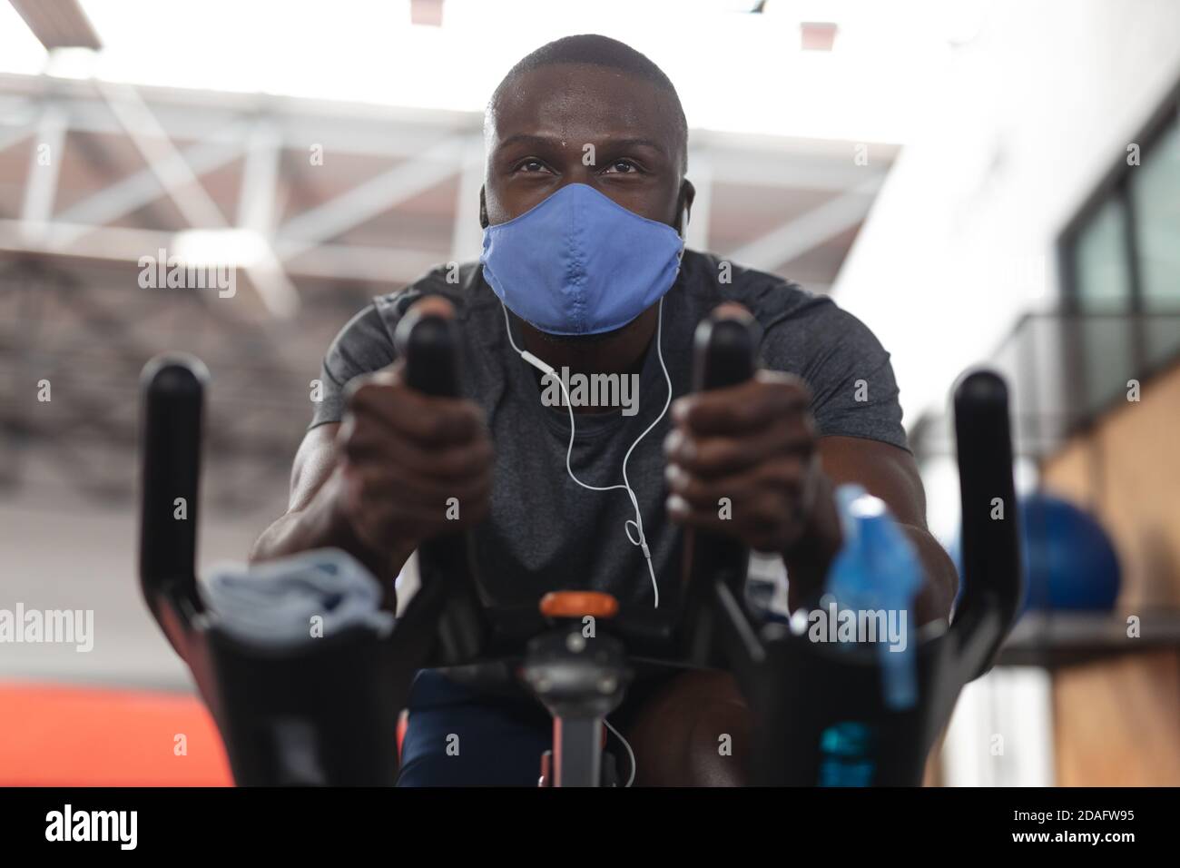 Fit Mann african american trägt Gesichtsmaske und Kopfhörer trainieren Auf dem Heimtrainer in der Turnhalle Stockfoto