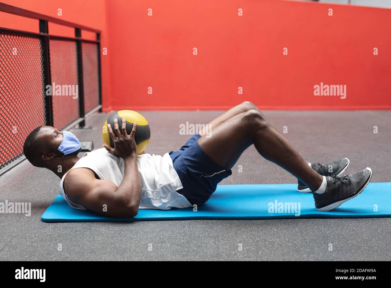Fit afroamerikanischen Mann trägt Gesichtsmaske Durchführung Übung mit Medizinball im Fitnessstudio Stockfoto