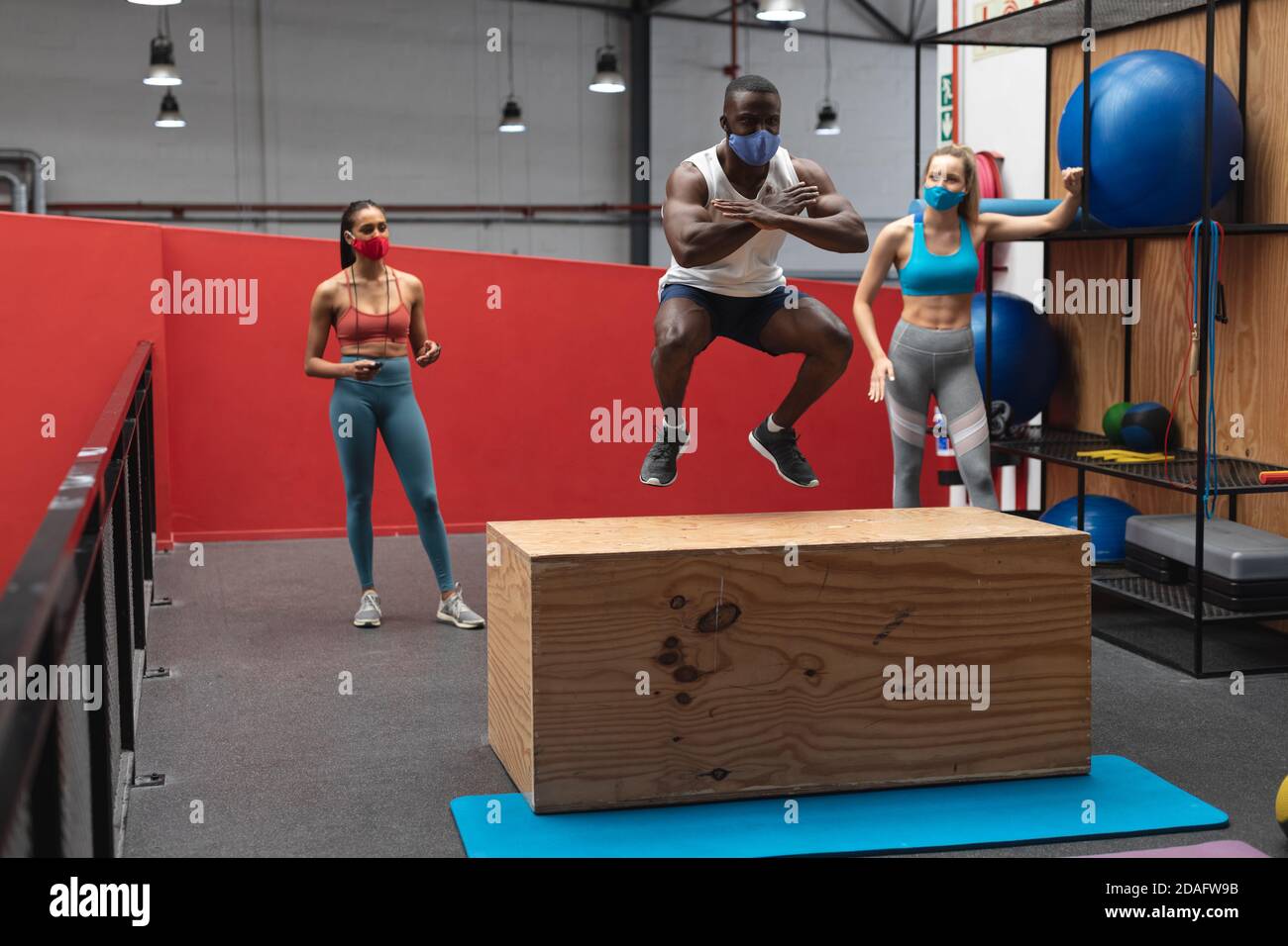 Fit afroamerikanischen Mann trägt Gesichtsmaske Springen auf Holz plyokasten im Fitnessraum während kaukasischen fe Stockfoto