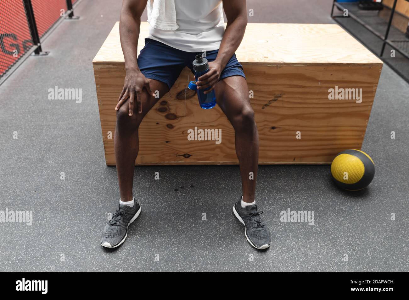 Mittelteil von fit afroamerikanischen Mann hält Wasserflasche Beim Sitzen auf hölzernen Plyokasten in der Stockfoto